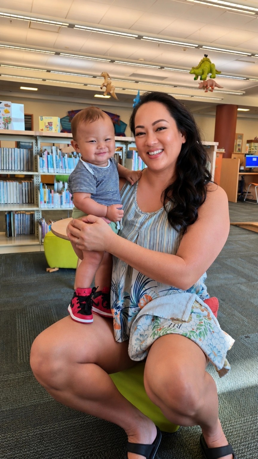 Leimomi holding a smiling Koa during a family library visit